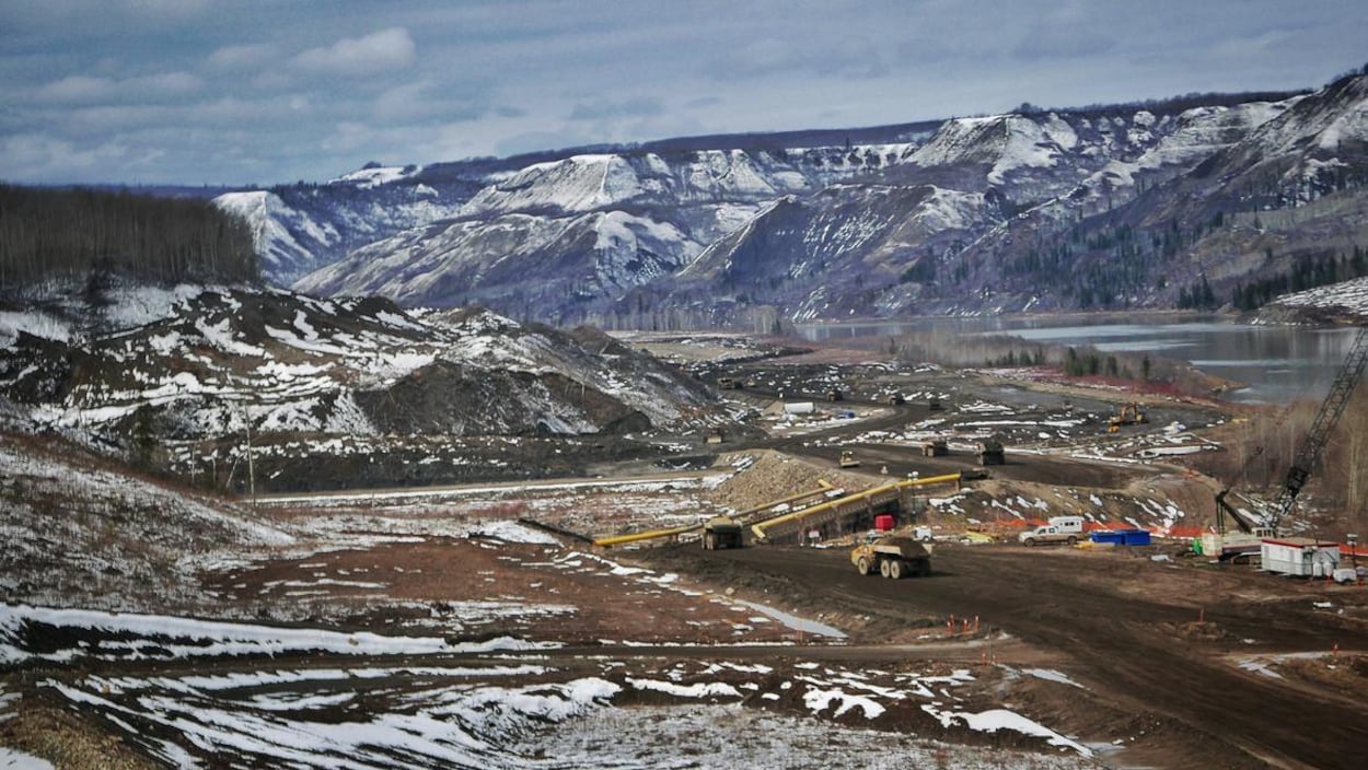 Plan panoramique d'un chantier de construction dans une vallée traversée par une rivière, le tout partiellement recouvert de neige.