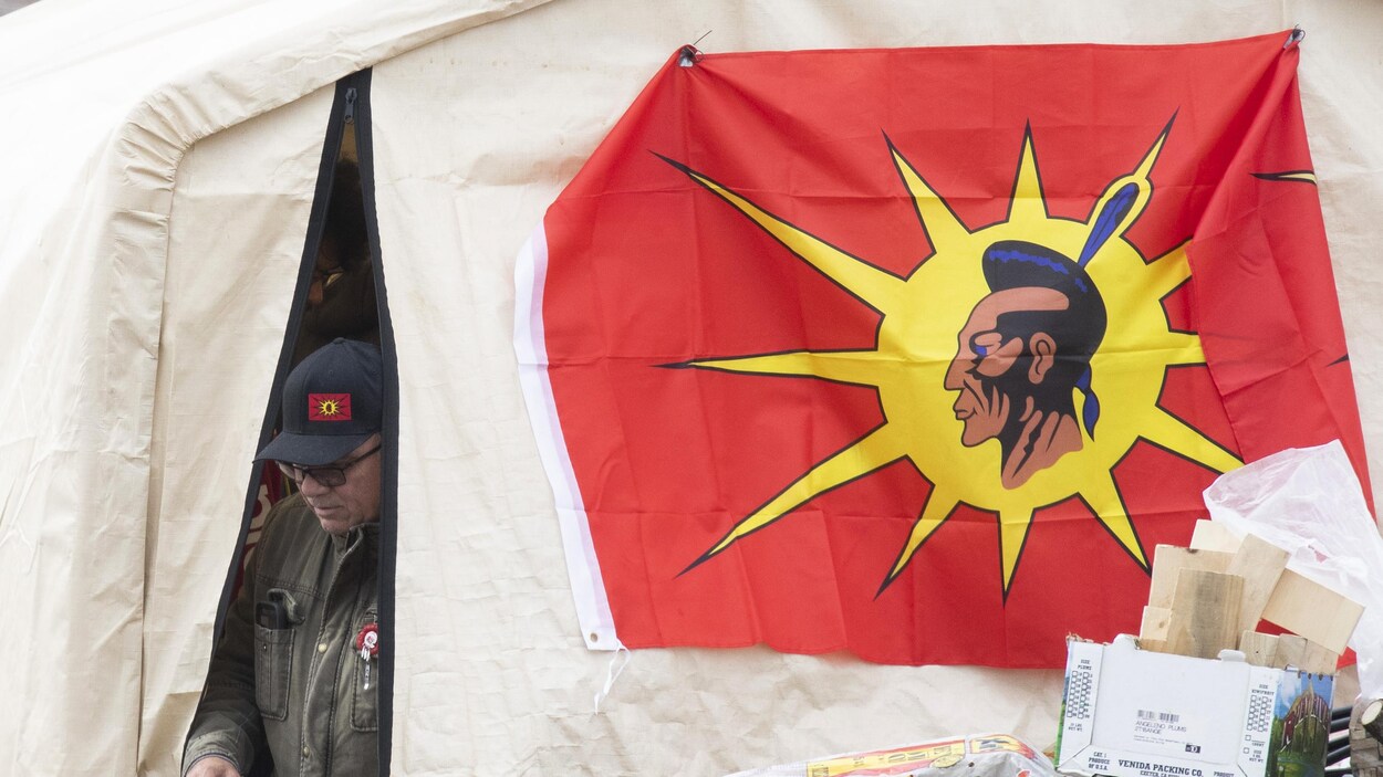 Un homme sort d'une tente à laquelle est accroché un drapeau mohawk.