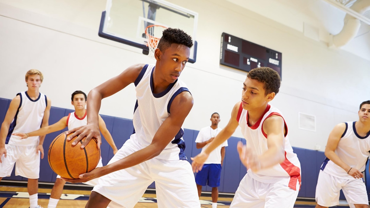 De jeunes hommes de l'école secondaire jouent au basketball dans un gymnase.