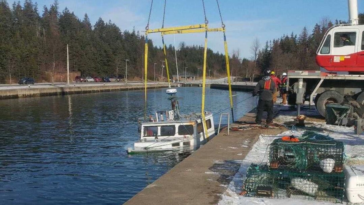 Une grue repêche un bateau coulé dont le toit sort de l'eau.