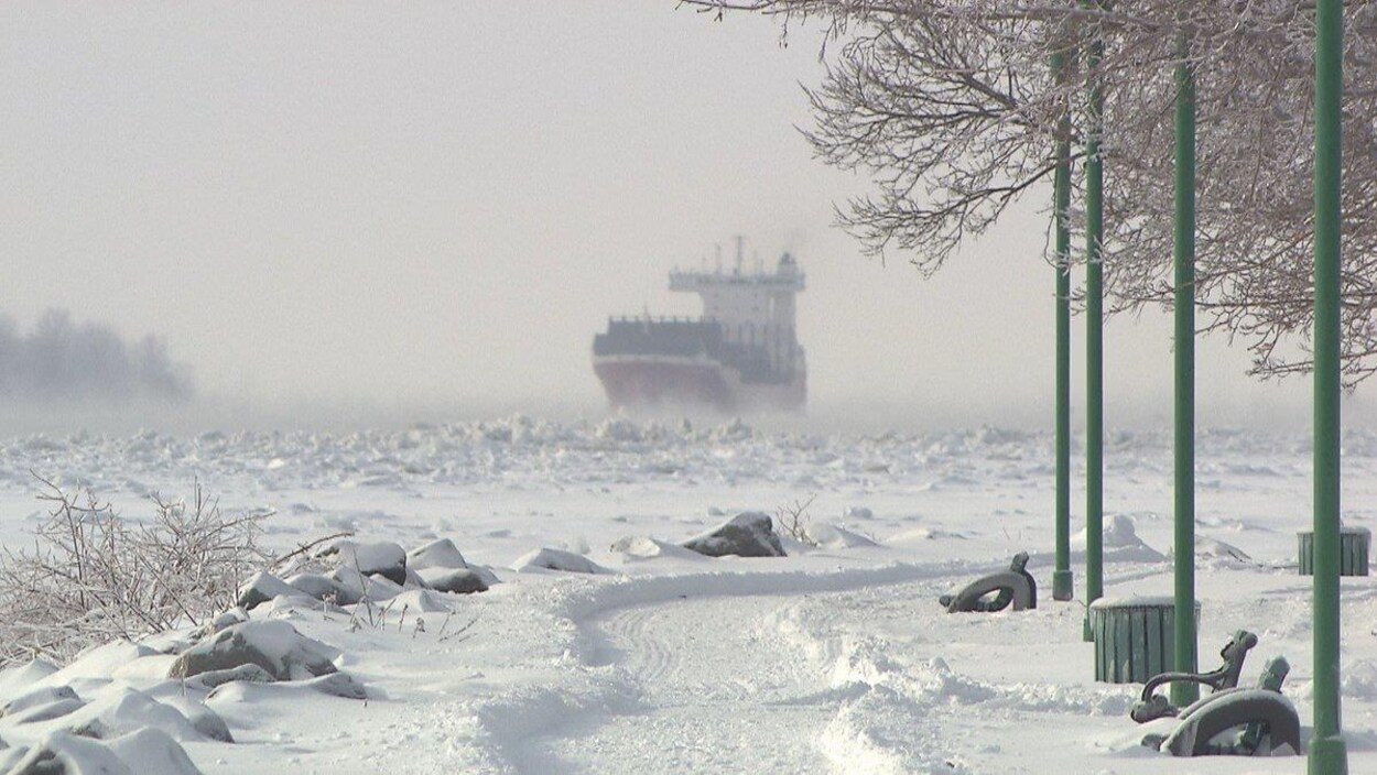 Un bateau, vu de la berge, navigue sur les eaux glacées du fleuve Saint-Laurent.