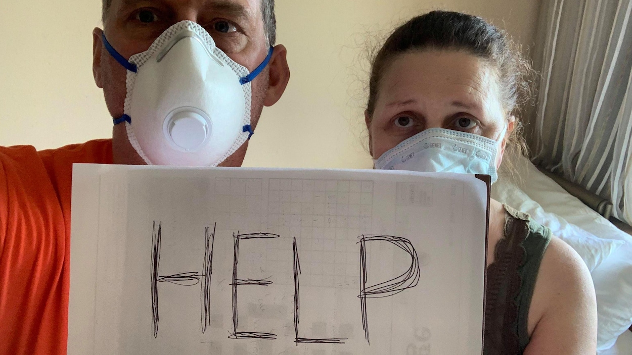Un homme et une femme dans une cabine de navire, portent des masques de protection et tiennent une feuille sur laquelle ils demandent de l'aide.