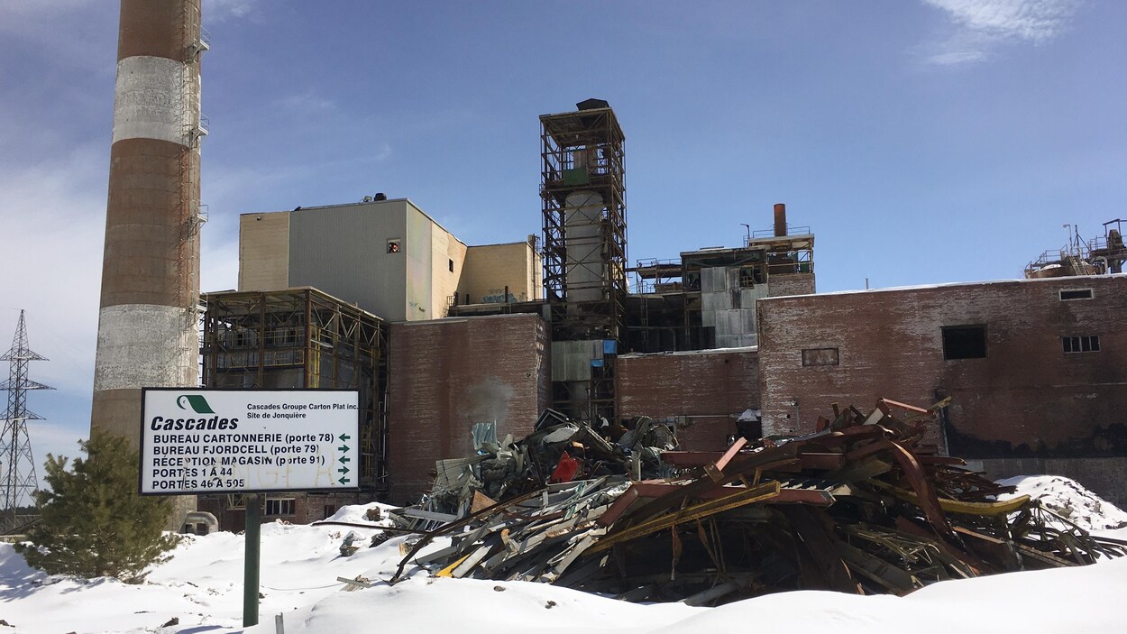 Une usine abandonnée avec des débris et une pancarte de l'ancienne Cascades devant.