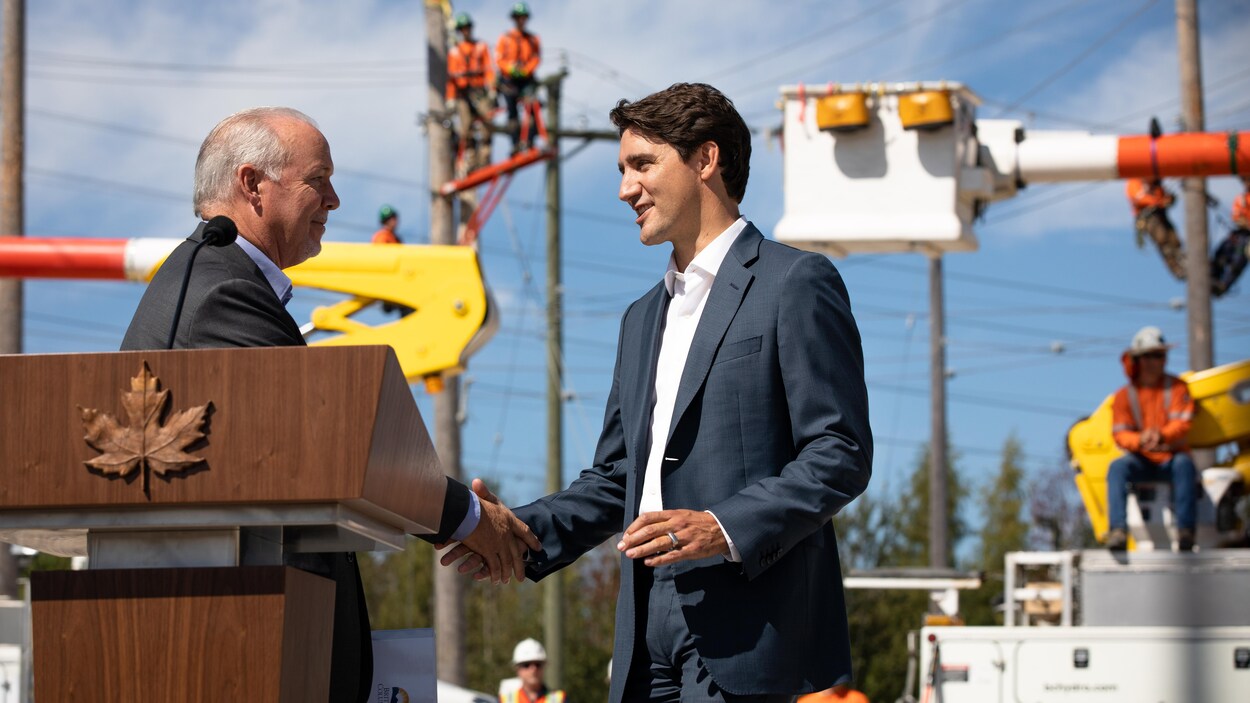 Justin Trudeau et John Horgan échangent une poignée de main devant des employés de BC Hydro, en arrière-plan.