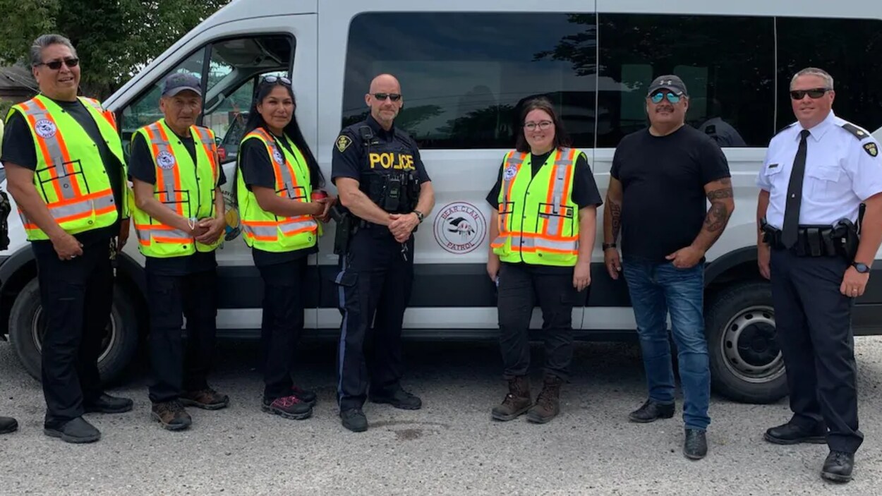 Cinq hommes et deux femmes en uniforme, devant une camionnette.