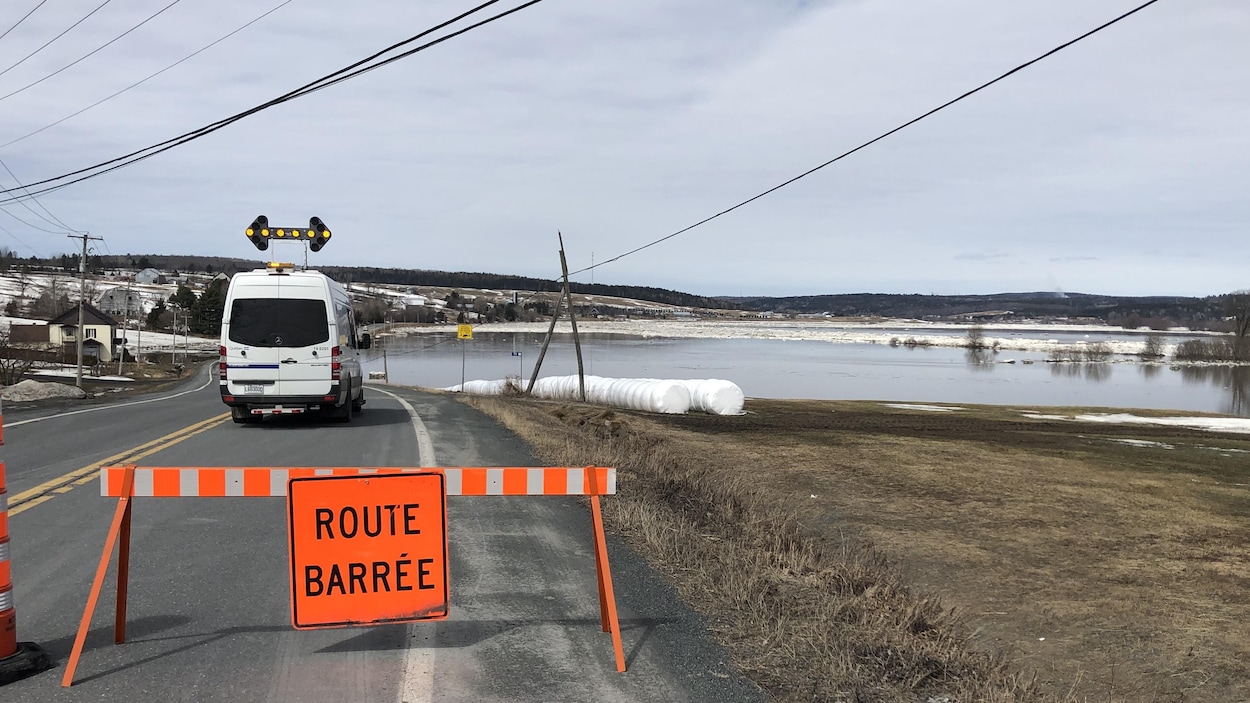 Un panneau signale une route barrée en avant-plan. À l'arrière-plan, la rivière Chaudière gonflée par la crue.