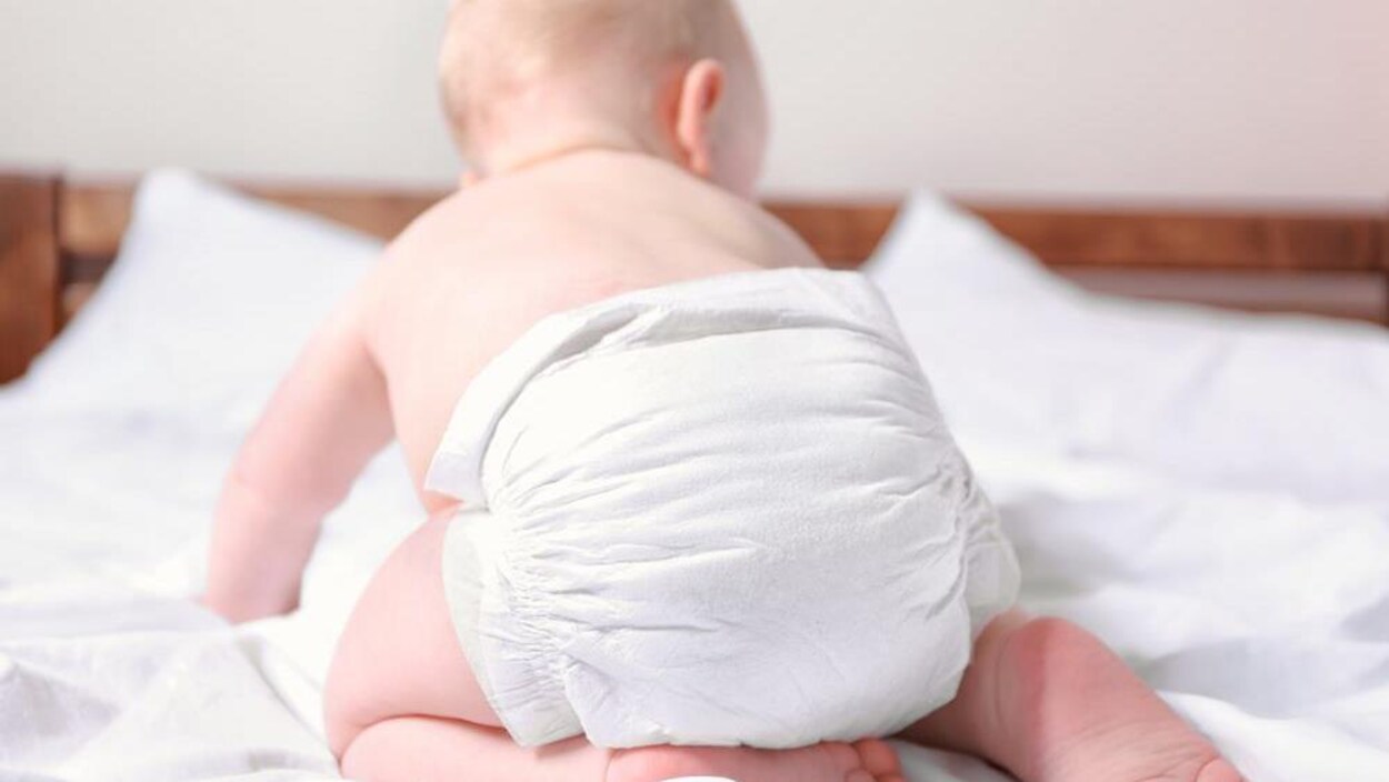 Un bébé blanc phtotographié de dos avec une couche blanche.