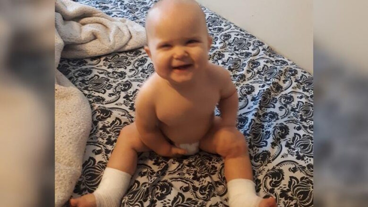Un bébé assis sur un lit. Il sourit.