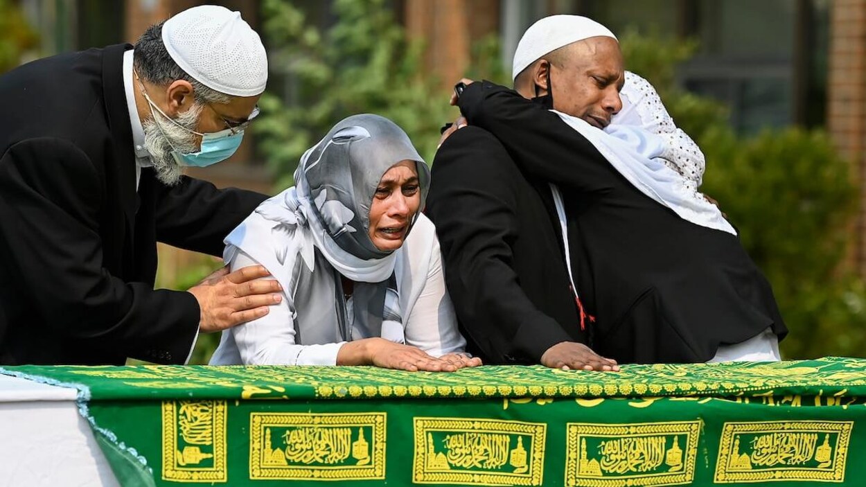 Quatre personnes devant un cercueil.