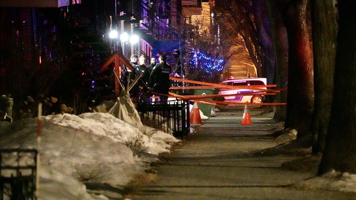 Quatre policiers se trouvent devant l'entrée d'un appartement, où un périmètre de sécurité est érigé.