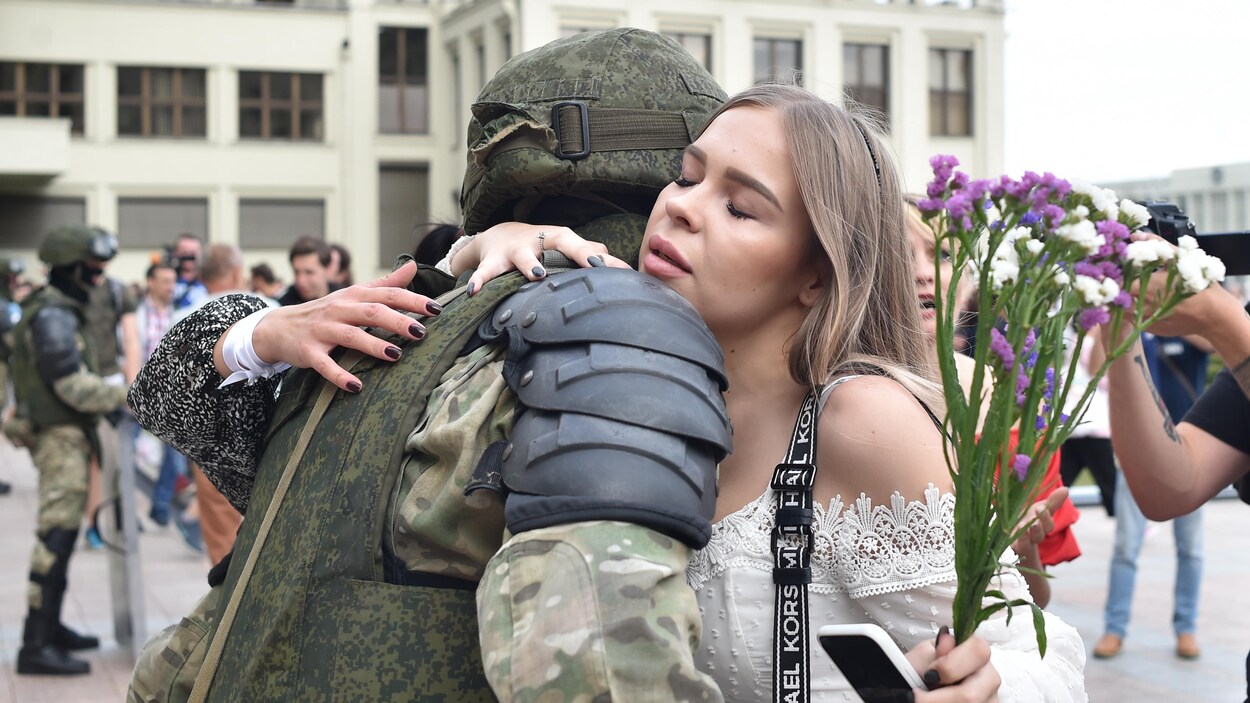 Une jeune femme tenant des fleurs serre un policier dans ses bras.