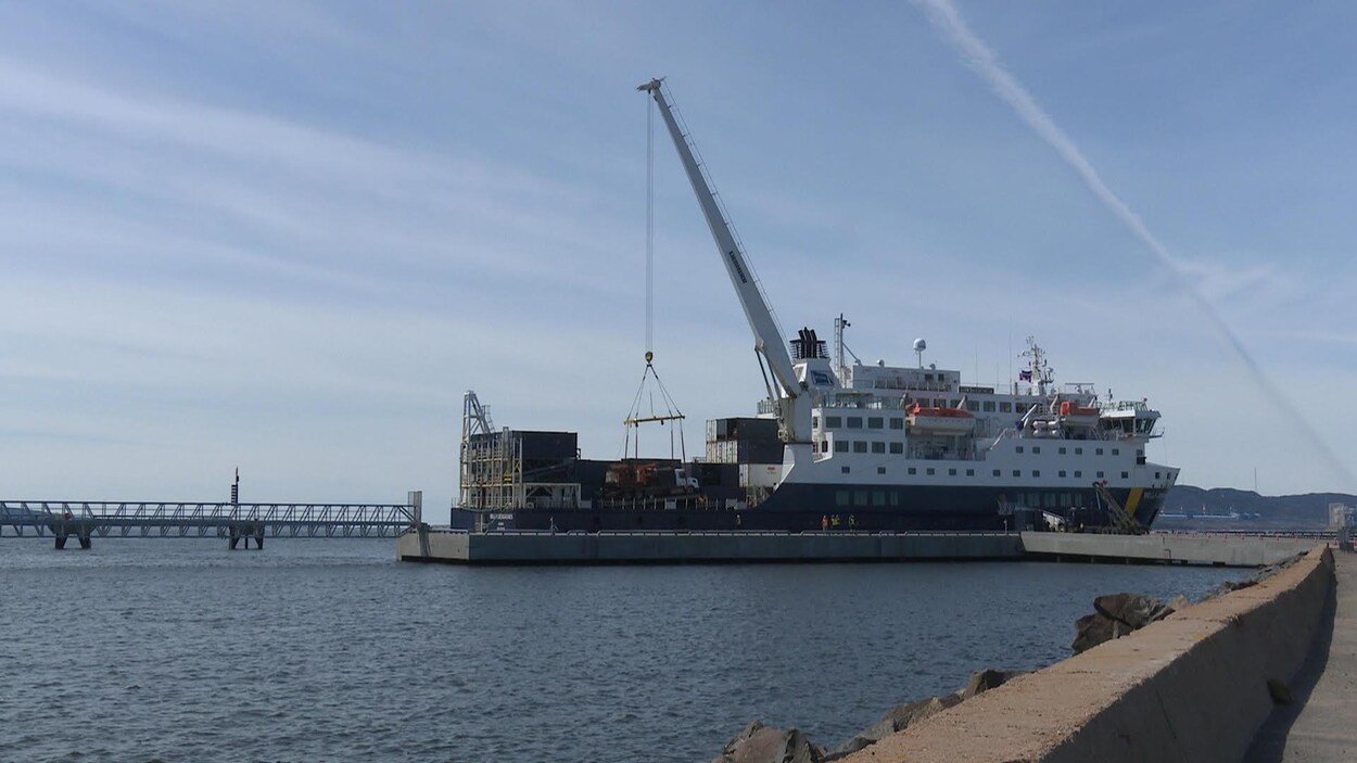 La grue déplace un camion vers l'intérieur du bateau accosté au quai.