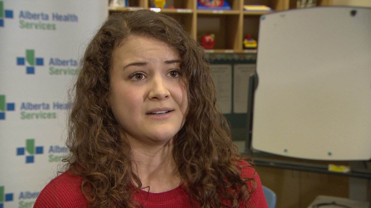 Une jeune femme aux cheveux bouclés. Elle porte un chandail rouge.