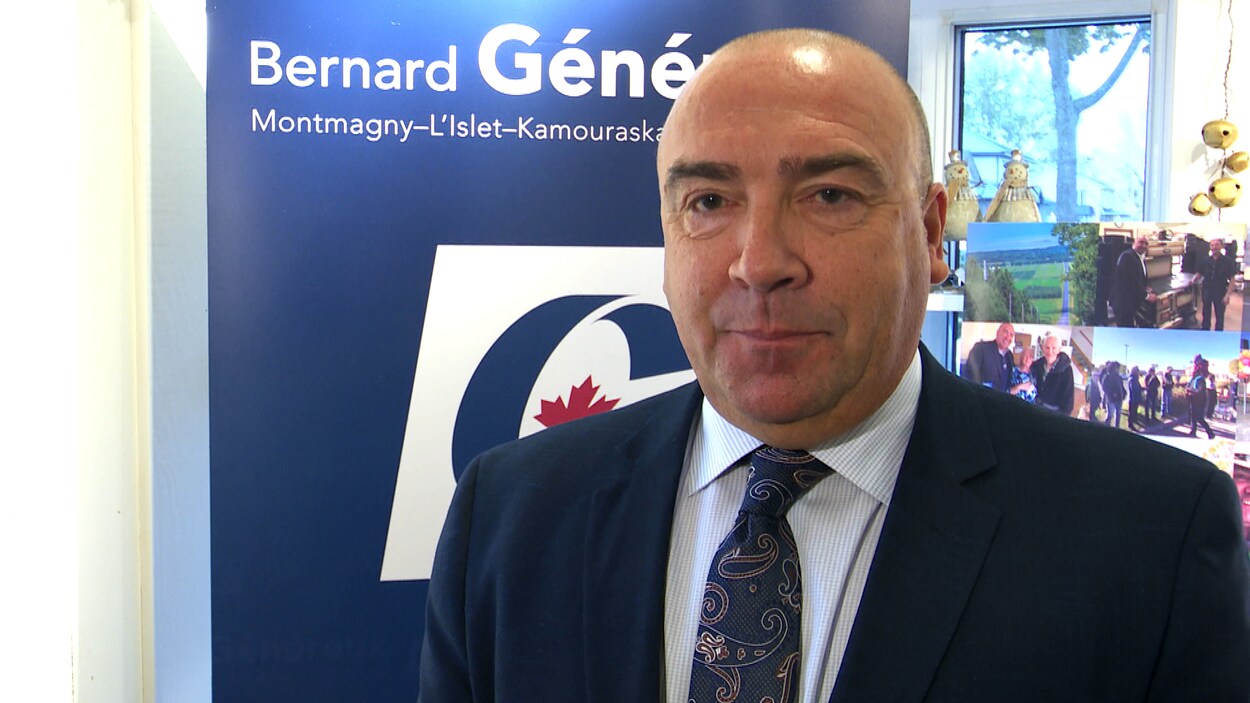 Bernard généreux pose devant une pancarte électorale.
