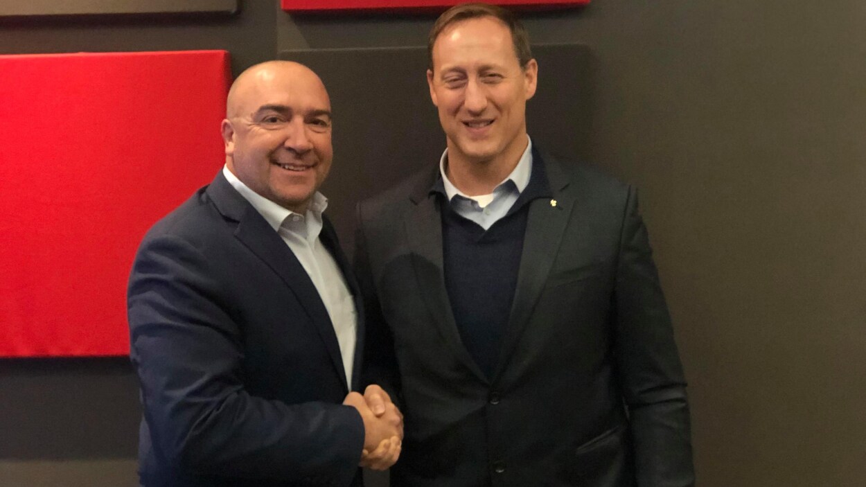 Les deux hommes se serrent la main en souriant à la caméra.