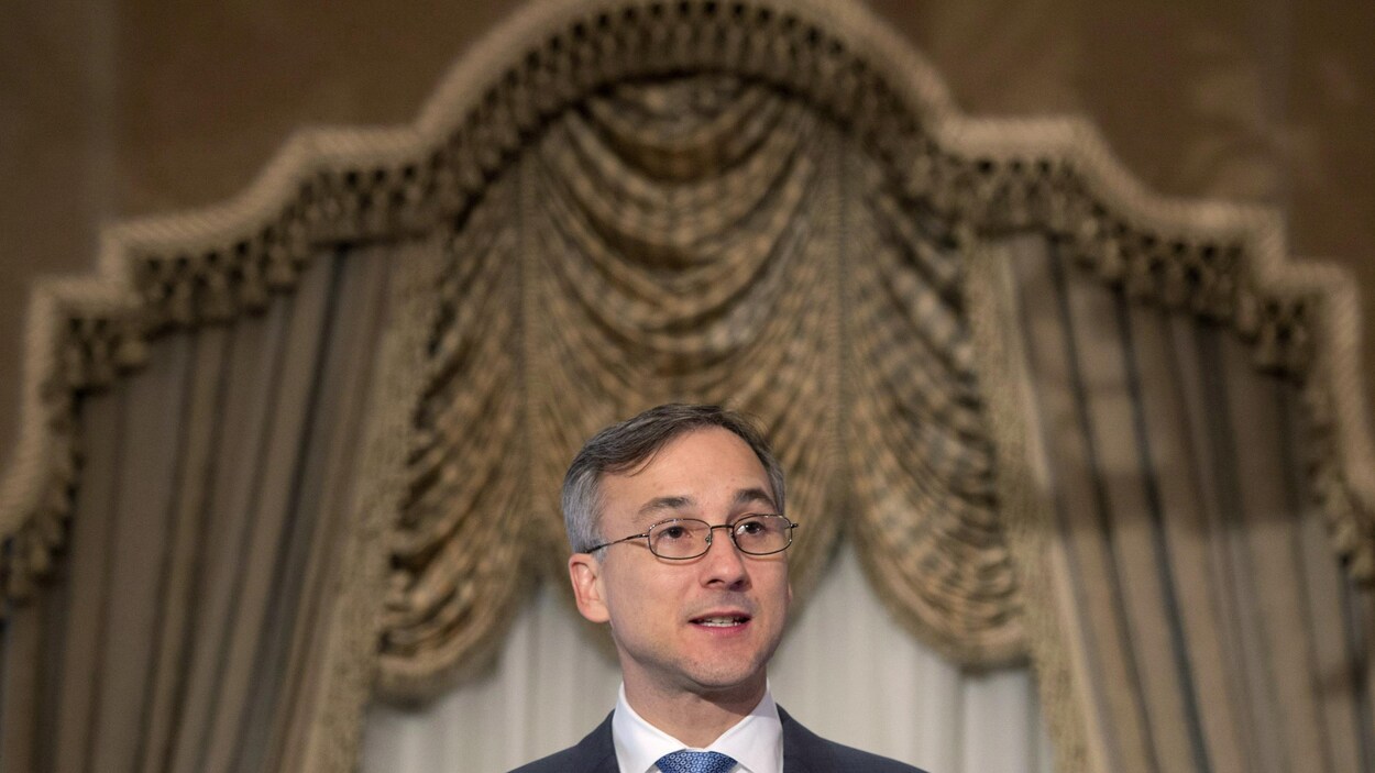 Un homme portant des lunettes parle sur une scène.