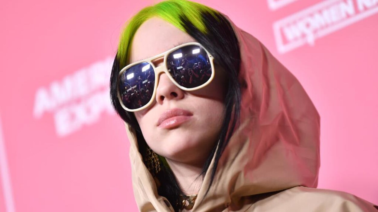 Billie Eilish porte des lunettes de soleil et ses cheveux noirs sont en partie teints en vert.