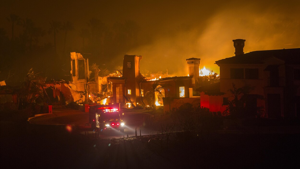 En pleine nuit, un feu de forêt brûle une maison devant laquelle se trouve un camion de pompiers.