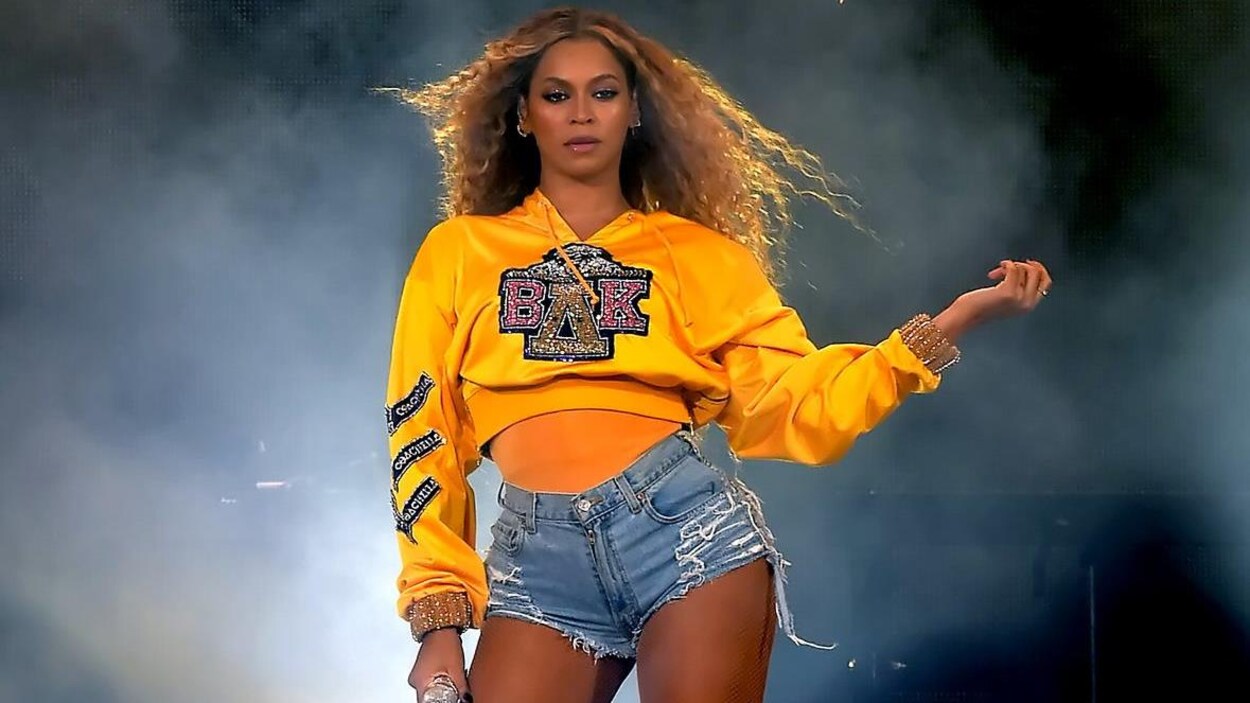 Beyonce porte un chandail jaune et un court short en jean.