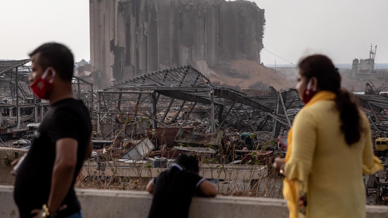 Des gens passent tandis que d'autres regardent les ruines du port de Beyrouth.