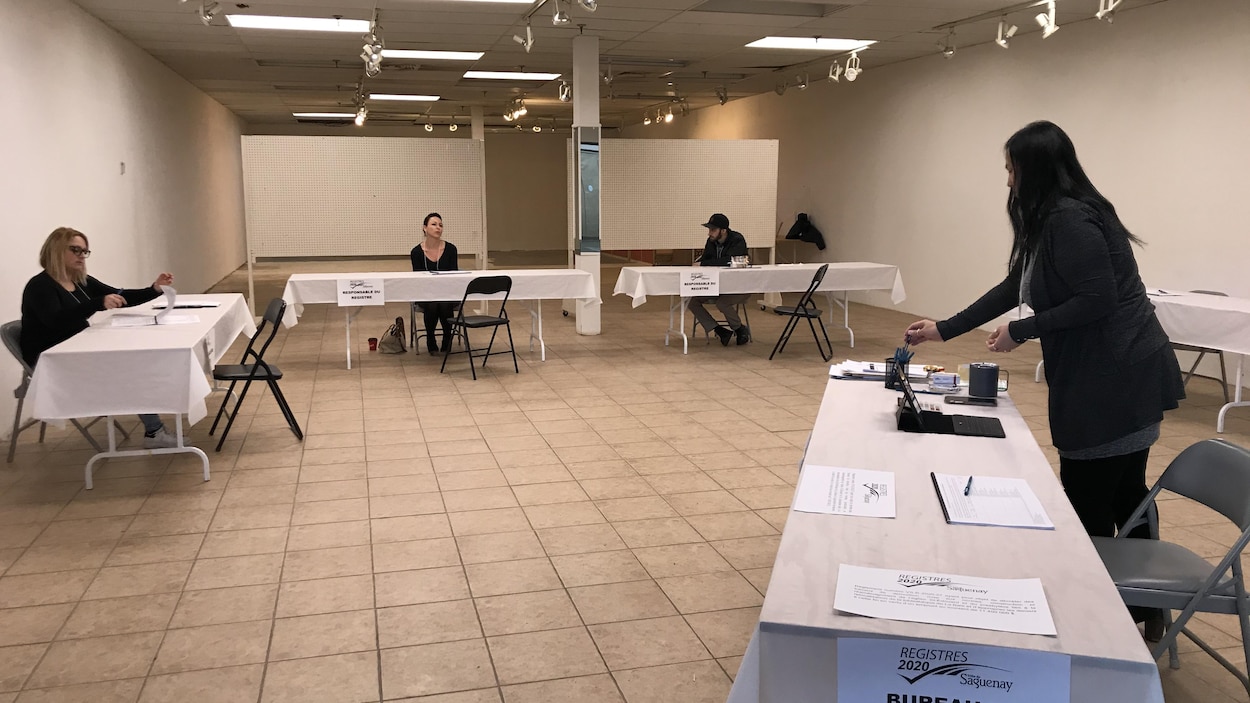 Trois personnes assises à trois tables dans une salle presque vide.