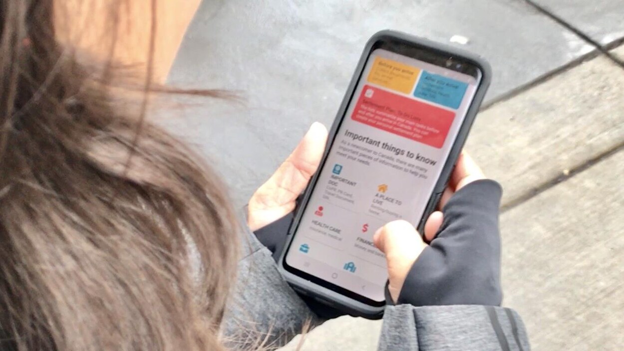 Une jeune femme tient un téléphone intelligent dans les mains. Elle regarde la première page de l'appli Welcome in Alberta.