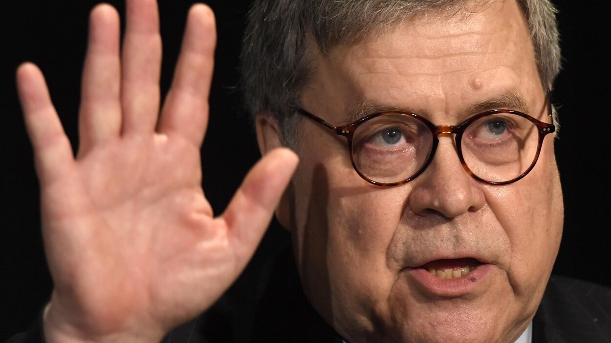Bill Barr regarde devant lui, la main levée.