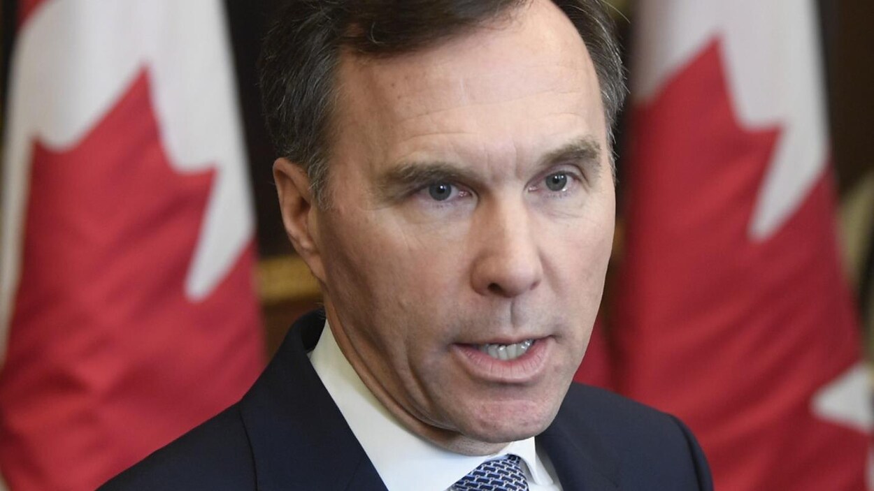 Plan rapproché de M. Morneau, devant des drapeaux du Canada.