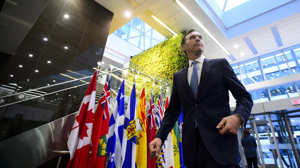 Bill Morneau marche devant les drapeaux du Canada, des provinces et des territoires.