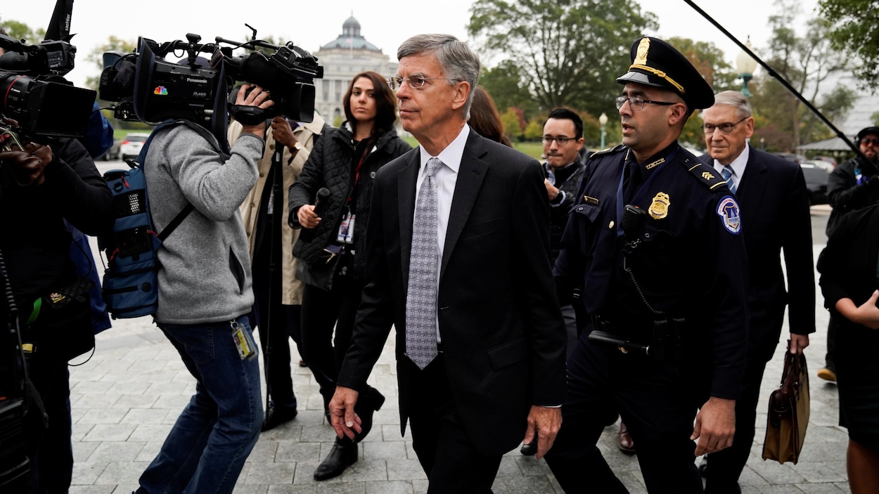 William Taylor marche en compagnie d'un policier parmi les journalistes.
