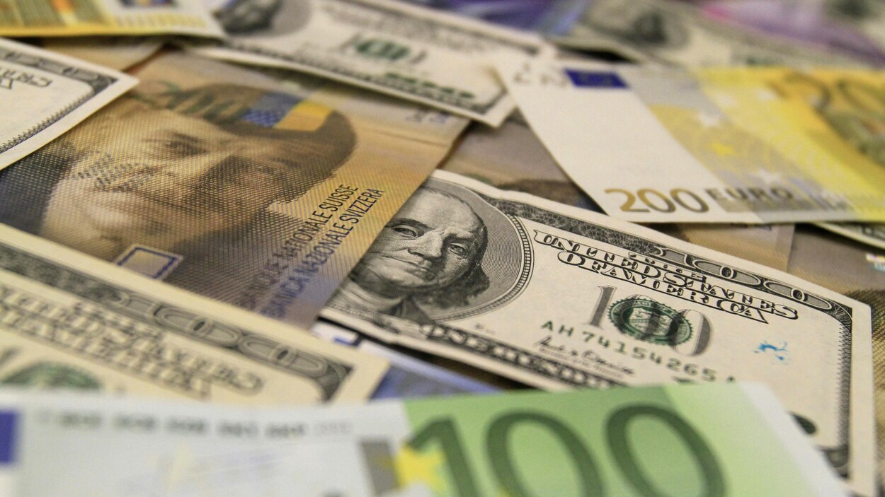 Des billets de banque en dollars américains, en euro et en francs suisses étalés sur une table.