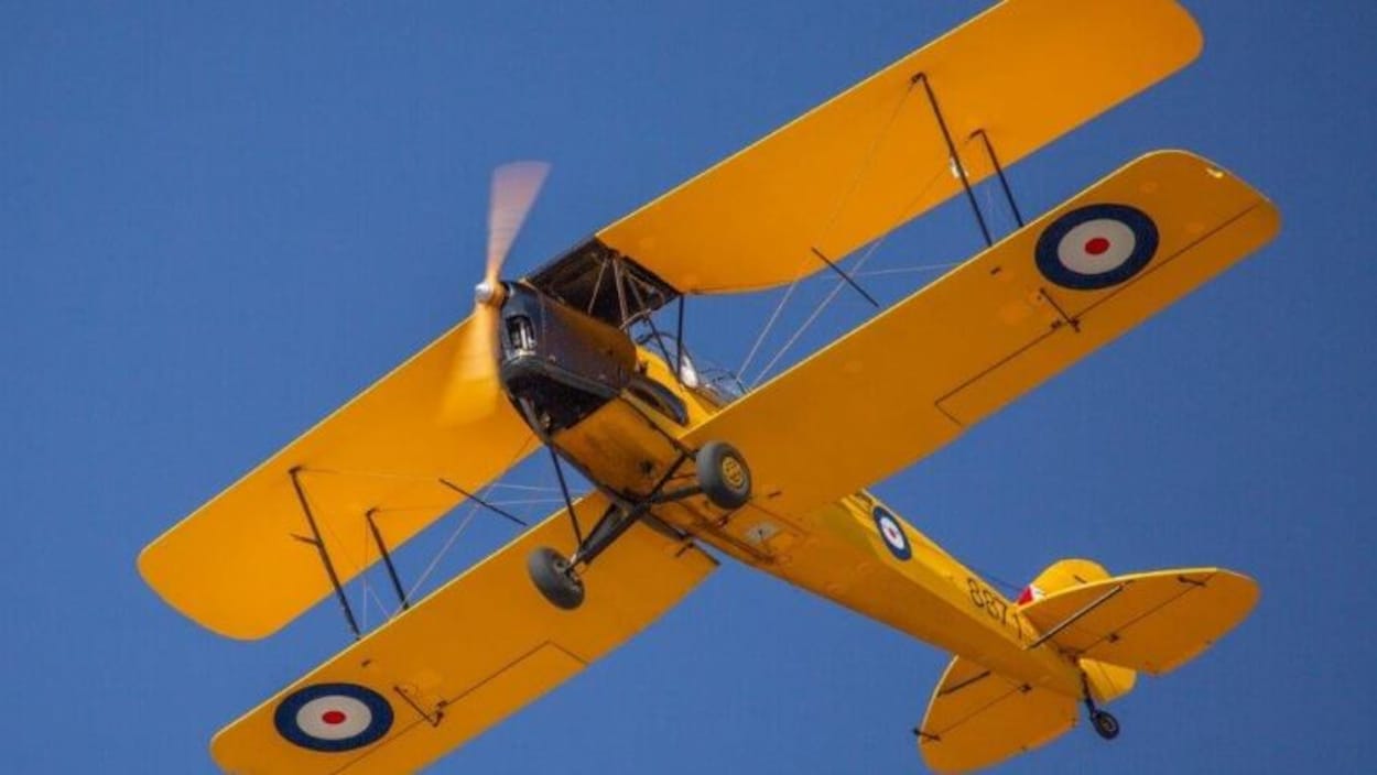 Le Tiger Moth restauré de 1942, un avion biplan volant dans un ciel sans nuages.