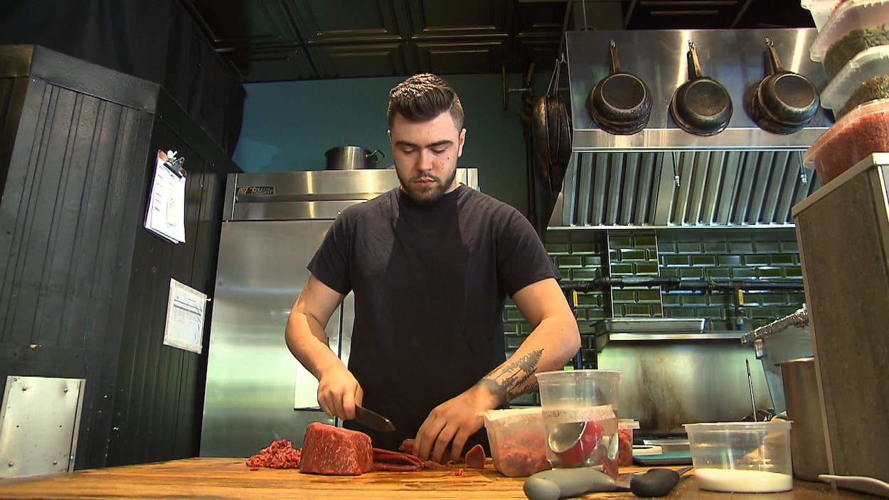 Un employé coupe un morceau de viande dans une cuisine. 