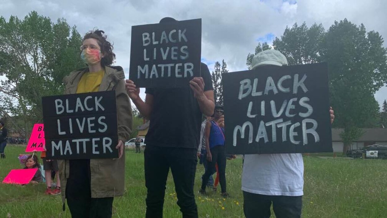Trois personnes tiennent des affiches sur lesquelles on peut lire en anglais : BLACK LIVES MATTER.