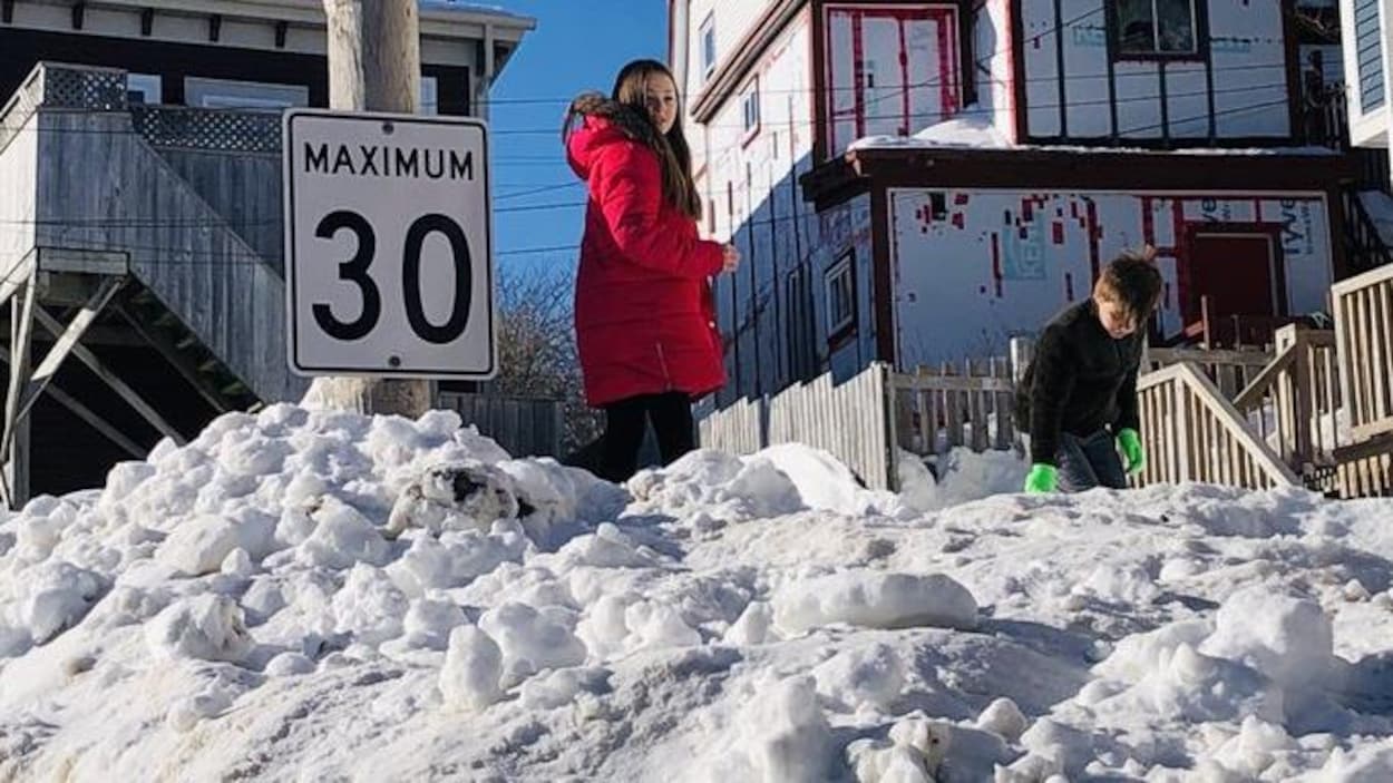 Deux enfants jouent au sommet d'un banc de neige à la même hauteur qu'un panneau de signalisation routière.