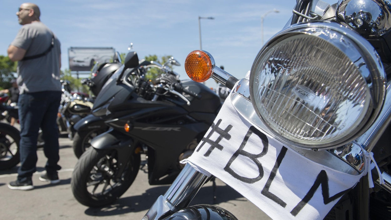 Plusieurs motos sont stationnées. Sur l'une d'elle, un morceau de tissu a été fixé sur lequel on peut lire BLM, les initiales de Black Lives Matter.