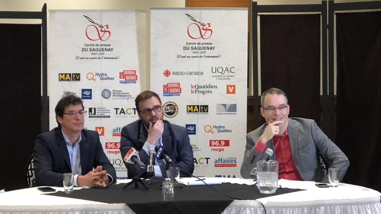 Trois hommes assis à une table discutent dans des micros.