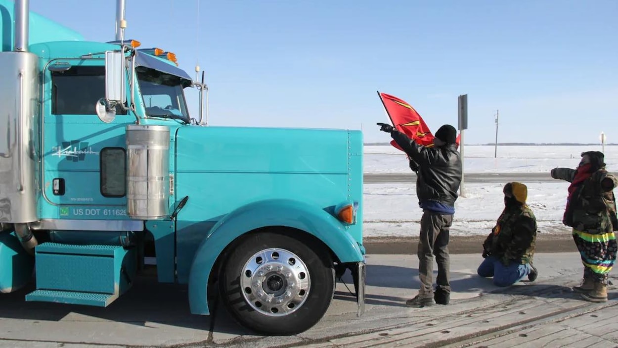 Un camion arrêté devant trois manifestants.