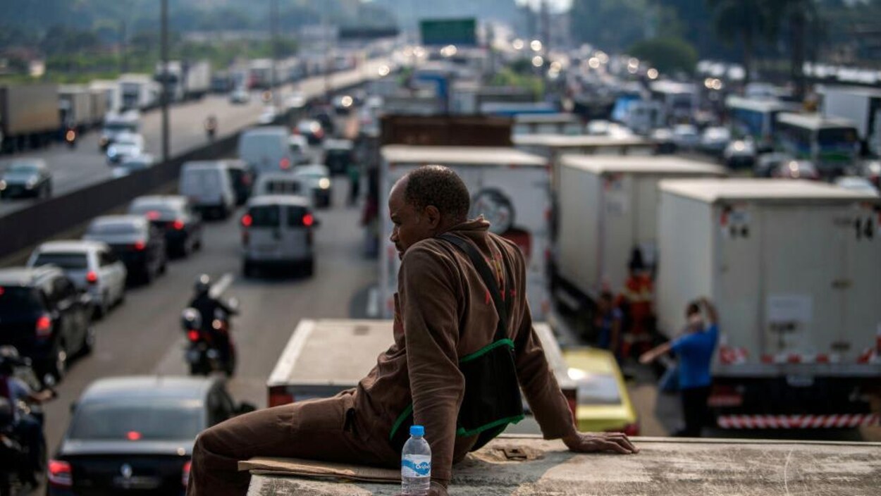 Un homme bloque partiellement la route et se repose sur son camion, avec une bouteille d'eau. Un homme bloque partiellement la route et se repose sur son camion, avec une bouteille d'eau.