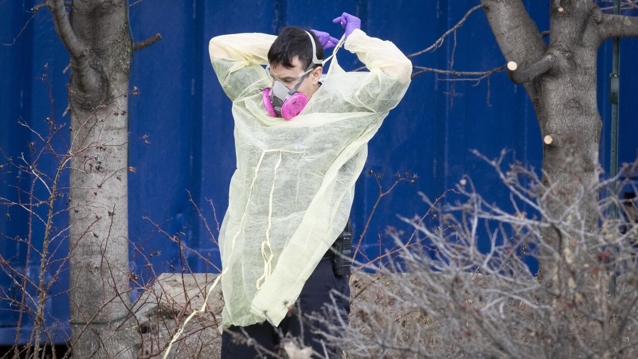 Un homme avec un masque enfile une blouse médicale.