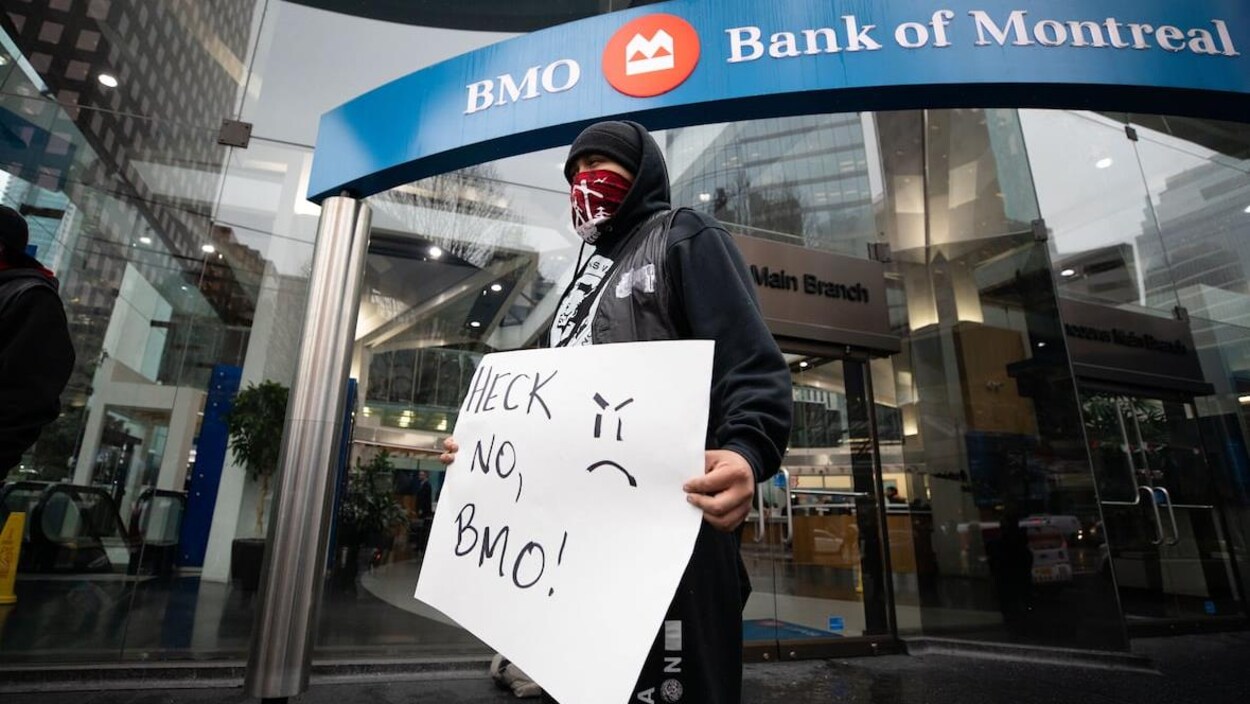 Des manifestants à la Banque de Montréal tenant une enseigne sur laquelle on lit « Non, BMO! » en anglais.