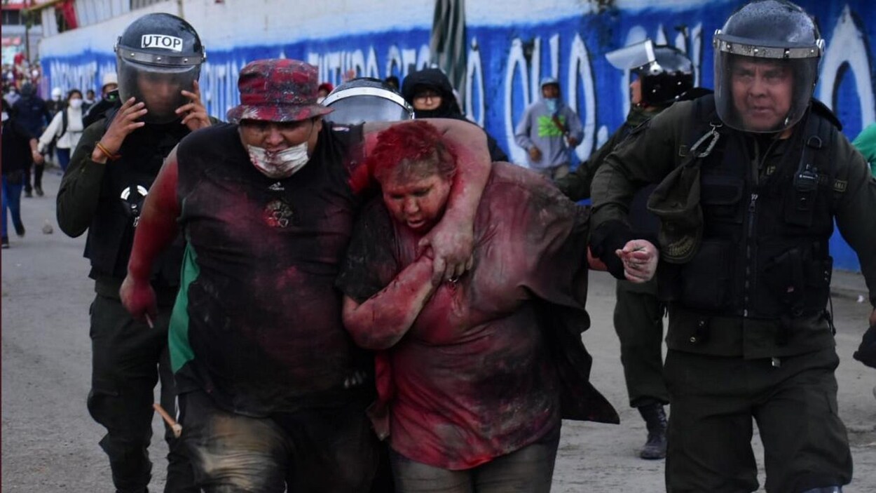 Patricia Arce couverte de peinture rouge escortée par des policiers.