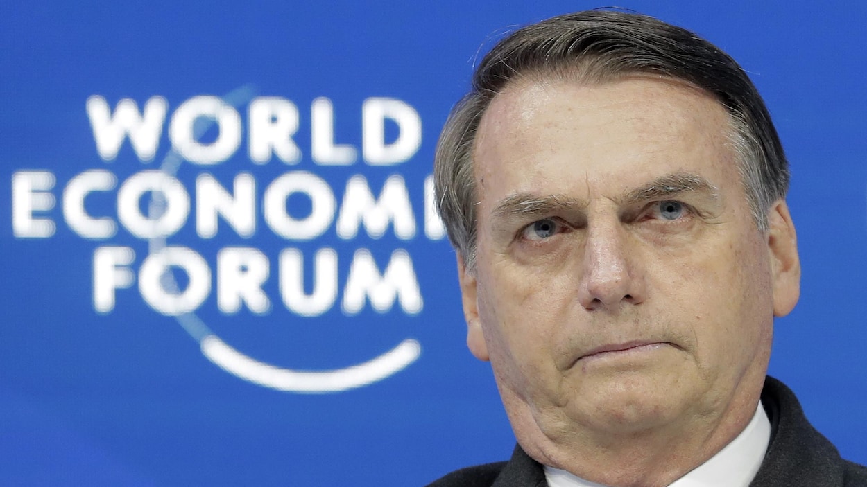 Gros plan du visage d'un homme avec en arrière-plan une murale sur laquelle on peut lire : World Economic Forum (Forum économique mondial).