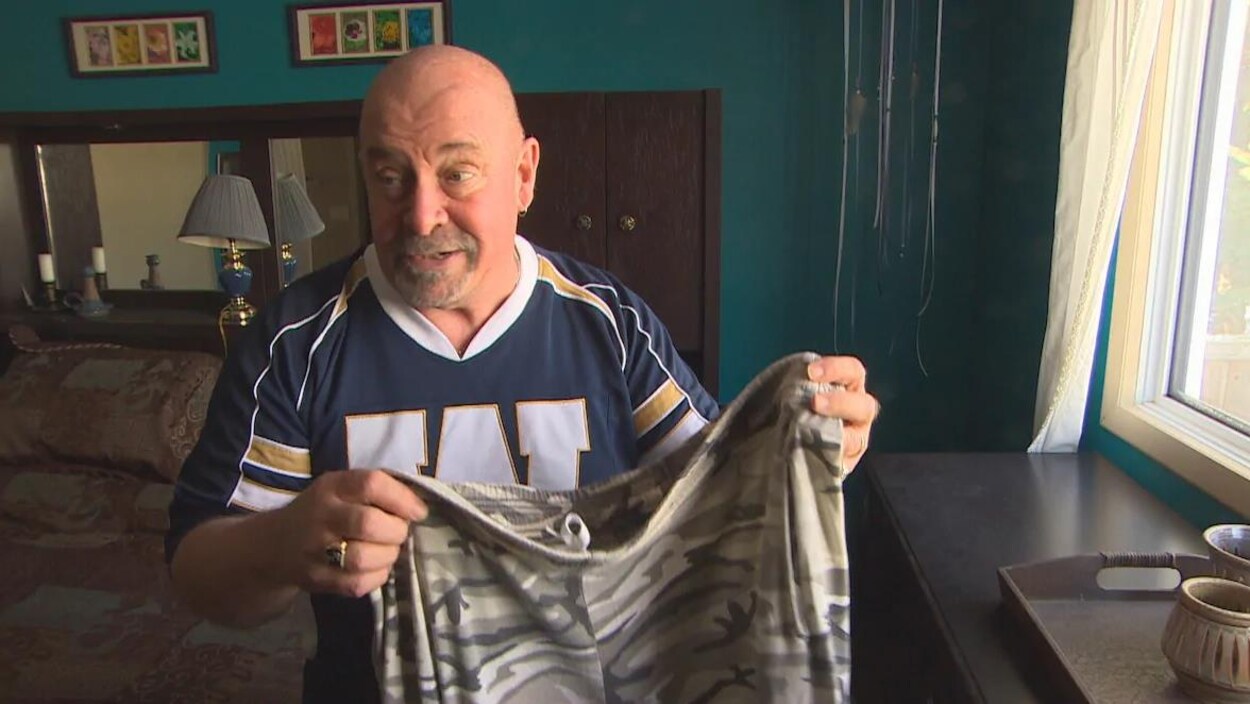 Un homme vêtu d'un chandail des Blue Bombers de Winnipeg tient dans ses mains un pantalon.