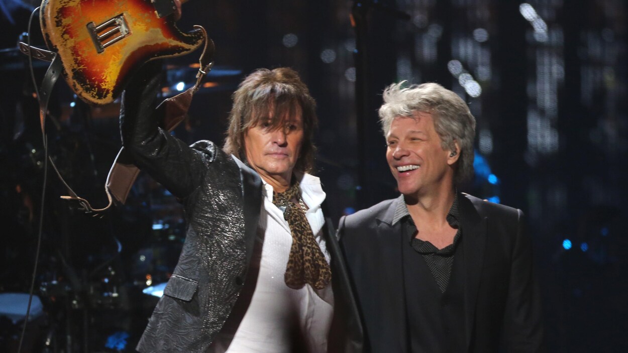 Le guitariste Richie Sambora lève sa guitare dans les airs alors qu'il fait l'accolade au chanteur Jon Bon Jovi sur scène lors de la cérémonie d'intronisation. Le guitariste Richie Sambora lève sa guitare dans les airs alors qu'il fait l'accolade au chanteur Jon Bon Jovi sur scène lors de la cérémonie d'intronisation.