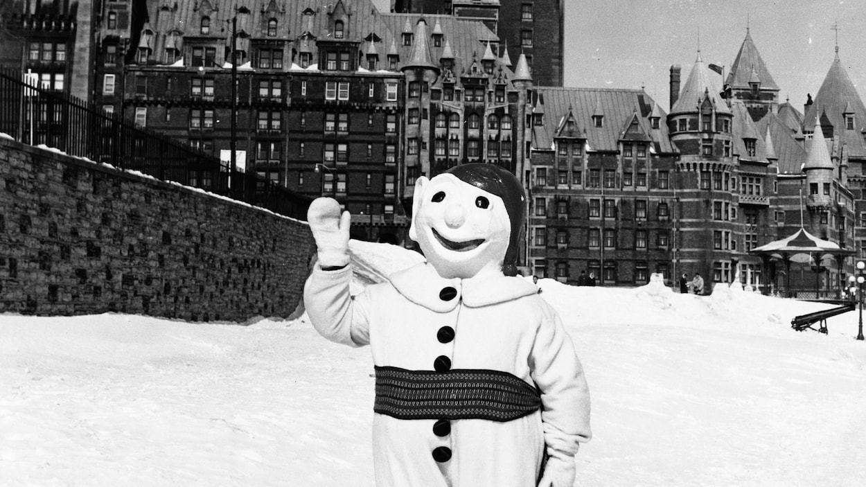 La mascotte se tient debout sur un sol enneigé, le Château Frontenac en arrière-plan.