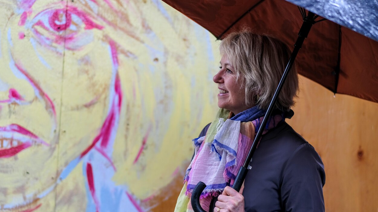 Sous un parapluie, la Dre Bonnie Henry regarde une série de peintures murales extérieures peintes par des artistes pour rendre hommage aux travailleurs de la santé dans le quartier Gastown, à Vancouver.