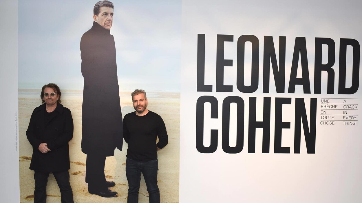 Les deux hommes posent devant une photo géante de Leonard Cohen, Les deux hommes posent devant une photo géante de Leonard Cohen,