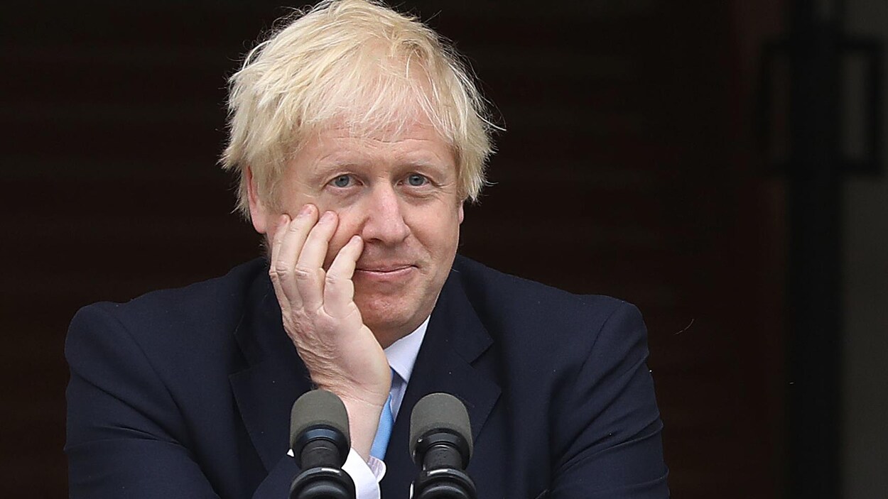 Boris Johnson place sa main droite sur son visage devant un lutrin.