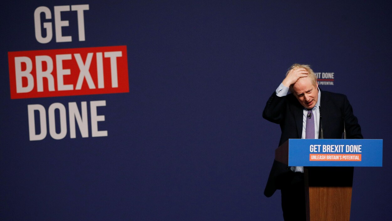 Boris Johnson est derrière un lutrin et passe sa main dans ses cheveux.
